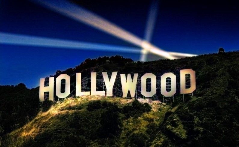 The iconic Hollywood sign illuminated at night against a dark blue sky with bright spotlights shining above.