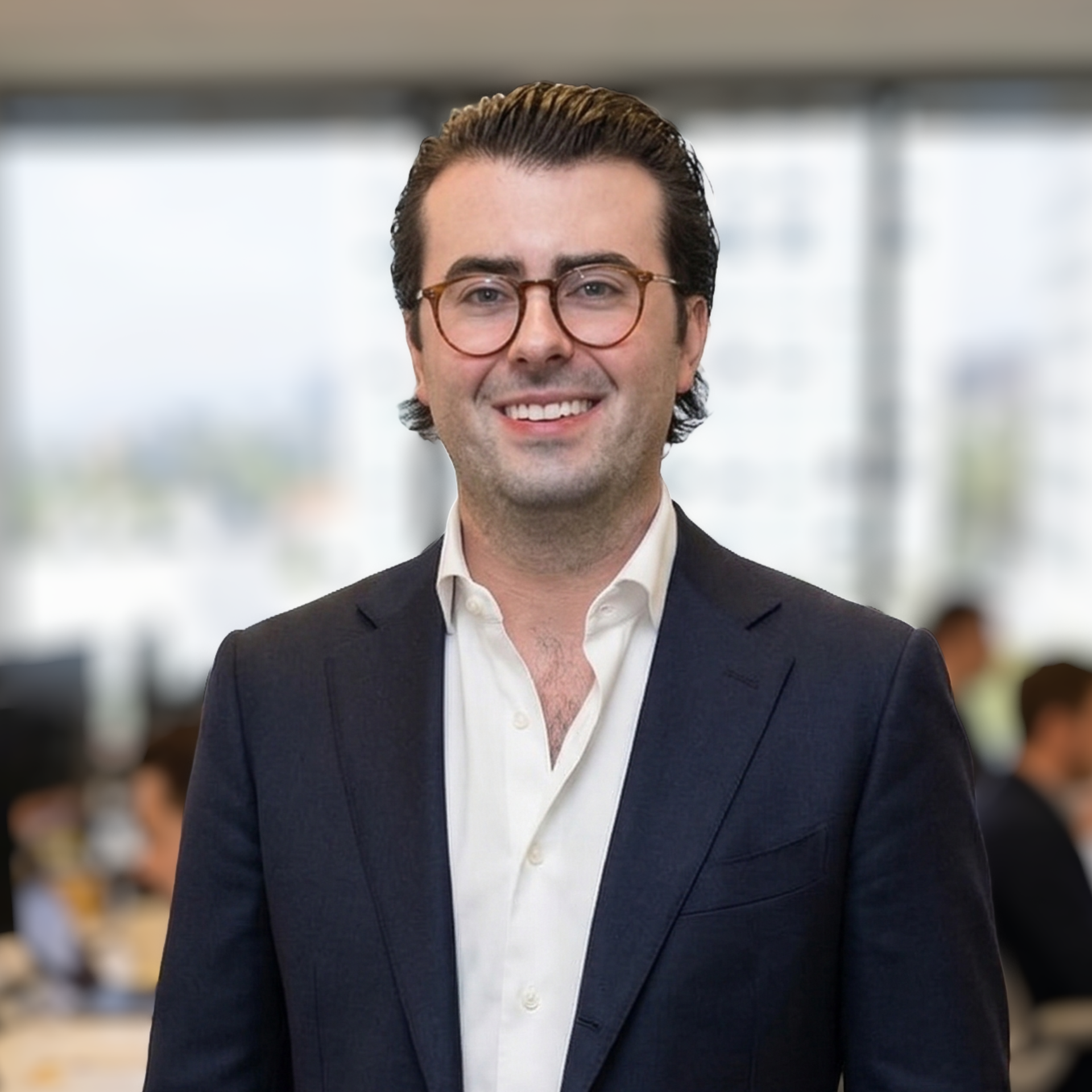 A professional headshot of a person wearing round-frame glasses and a navy blazer with an open-collared white shirt.