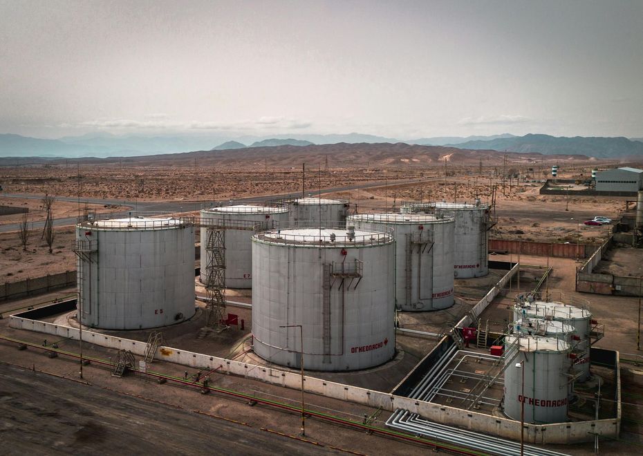A group of large, cylindrical metal industrial storage tanks situated in a vast, arid, desert landscape.