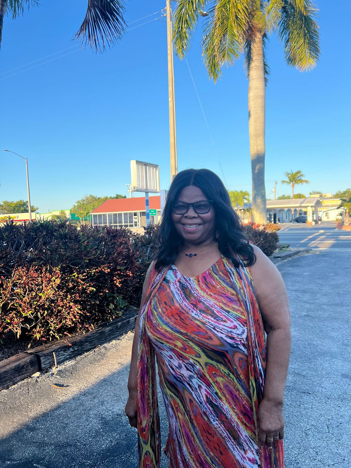 A woman in a colorful dress stands in front of palm trees