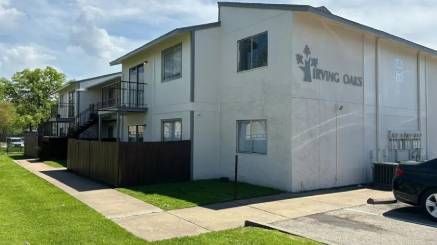 A white apartment building with a car parked in front of it.