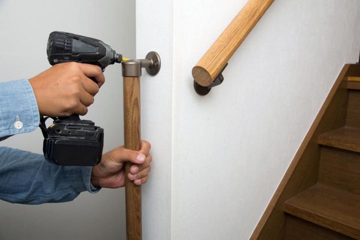 A man is installing a wooden handrail on a staircase with a drill.
