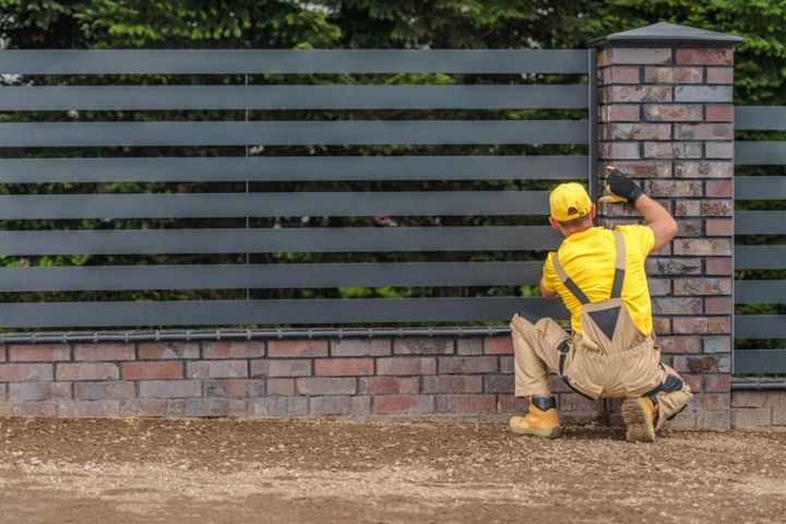 A man is installing a fence on a brick wall.