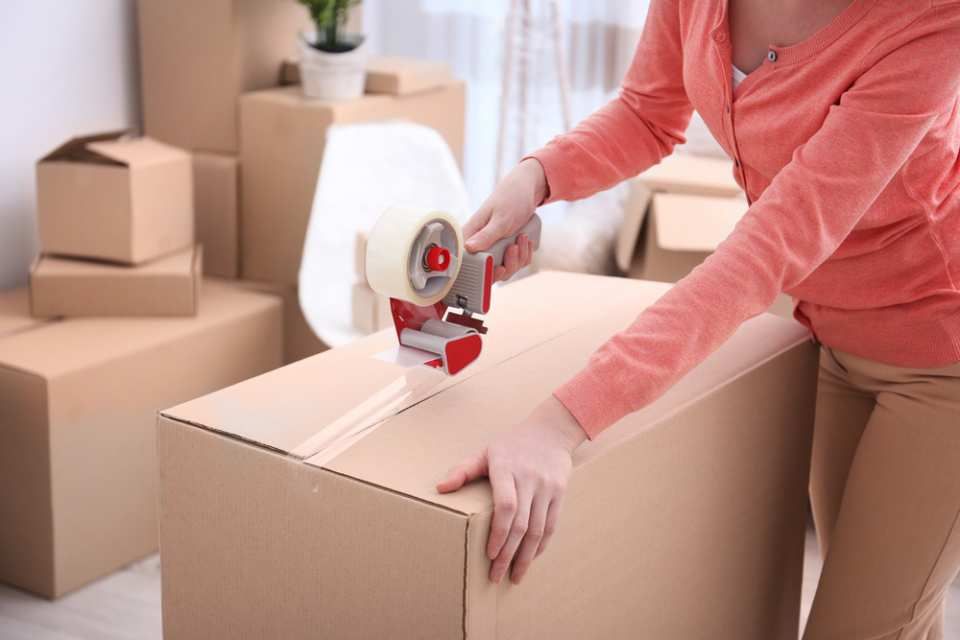 A woman is taping a cardboard box with tape.