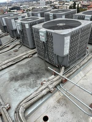 Row of large gray HVAC rooftop units on a commercial building rooftop with visible pipes and ducts.