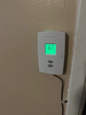 Wall thermostat with green digital display reading 67 on a beige wall.