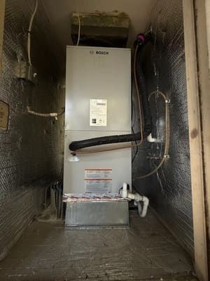 Water heater or furnace unit in a reflective insulated utility closet with pipes and wiring.