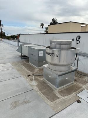 Rooftop HVAC units and ductwork on a flat commercial roof under an overcast sky