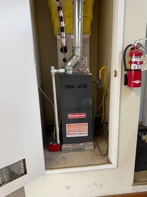 Basement furnace in a utility closet with exposed ductwork and a red fire extinguisher on the right