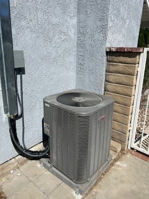 Outdoor air conditioning unit beside a stucco wall and fence on a concrete patio