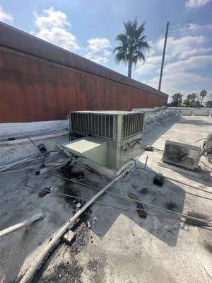 Rooftop HVAC unit beside a tall red wall, with scattered cables and debris under a cloudy sky.