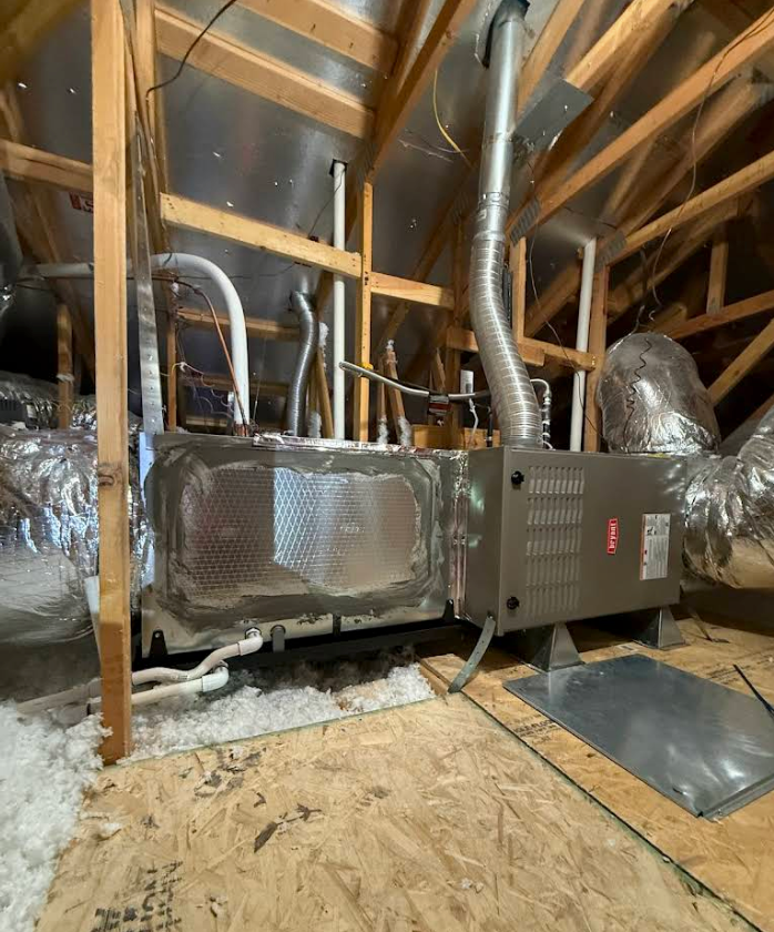 Attic HVAC unit with ductwork and insulation amid exposed wooden rafters