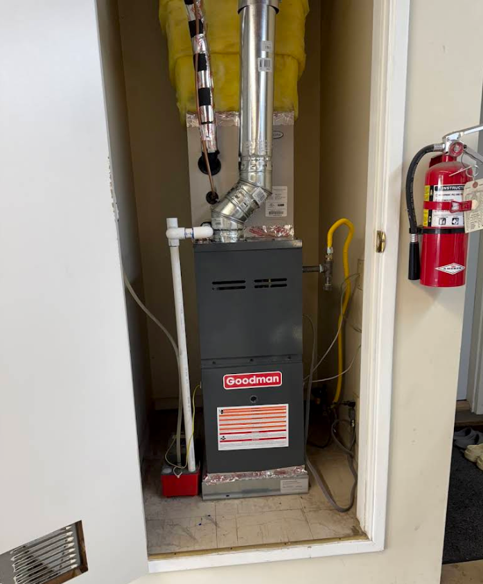 Gas furnace in a utility closet with silver ducting and a red fire extinguisher beside it.