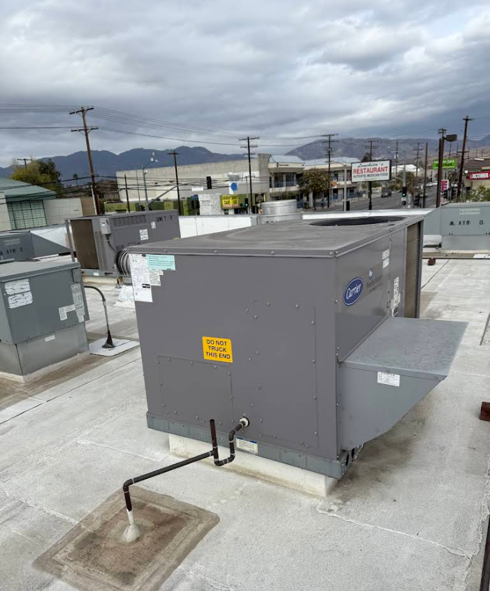 Gray rooftop HVAC unit with side vents on a commercial roof under a cloudy sky