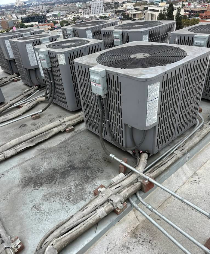 Rooftop row of large gray HVAC units with pipes and ducts in an industrial setting