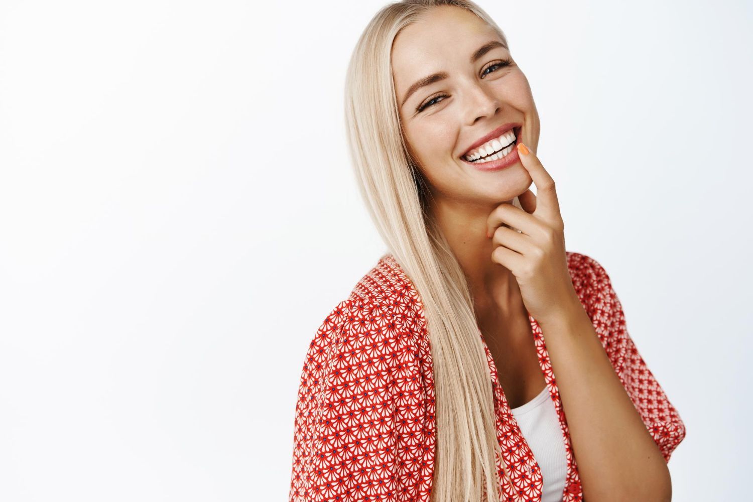 A woman with long blonde hair is smiling with her hand on her chin.