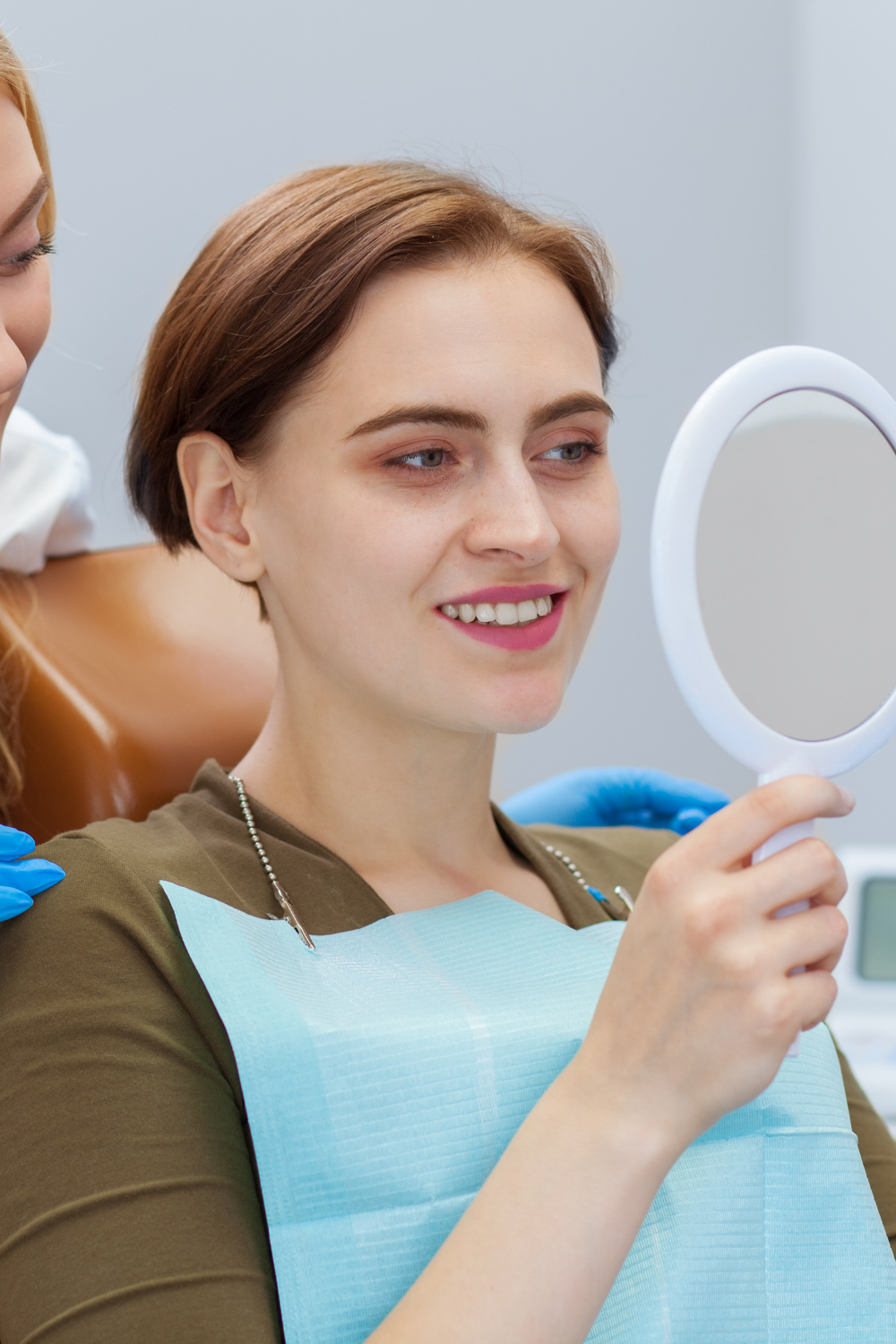 A woman is looking at her teeth in a mirror at the dentist.