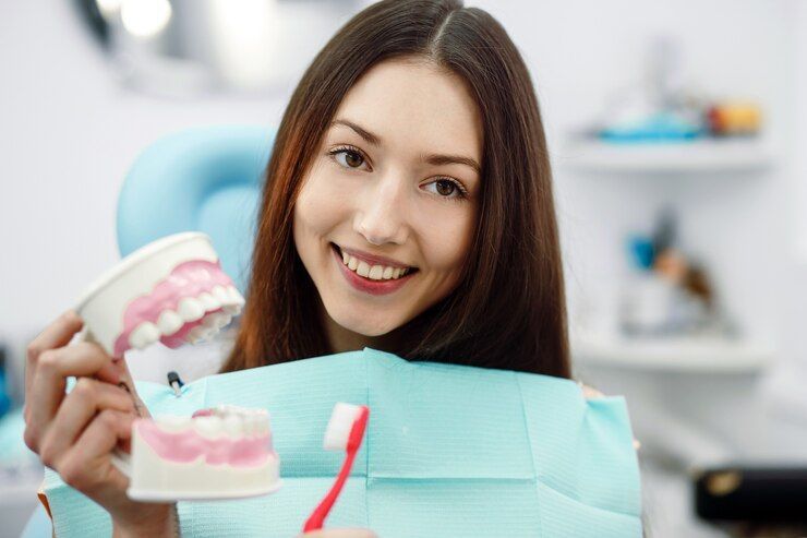 A woman is sitting in a dental chair holding a model of teeth and a toothbrush.