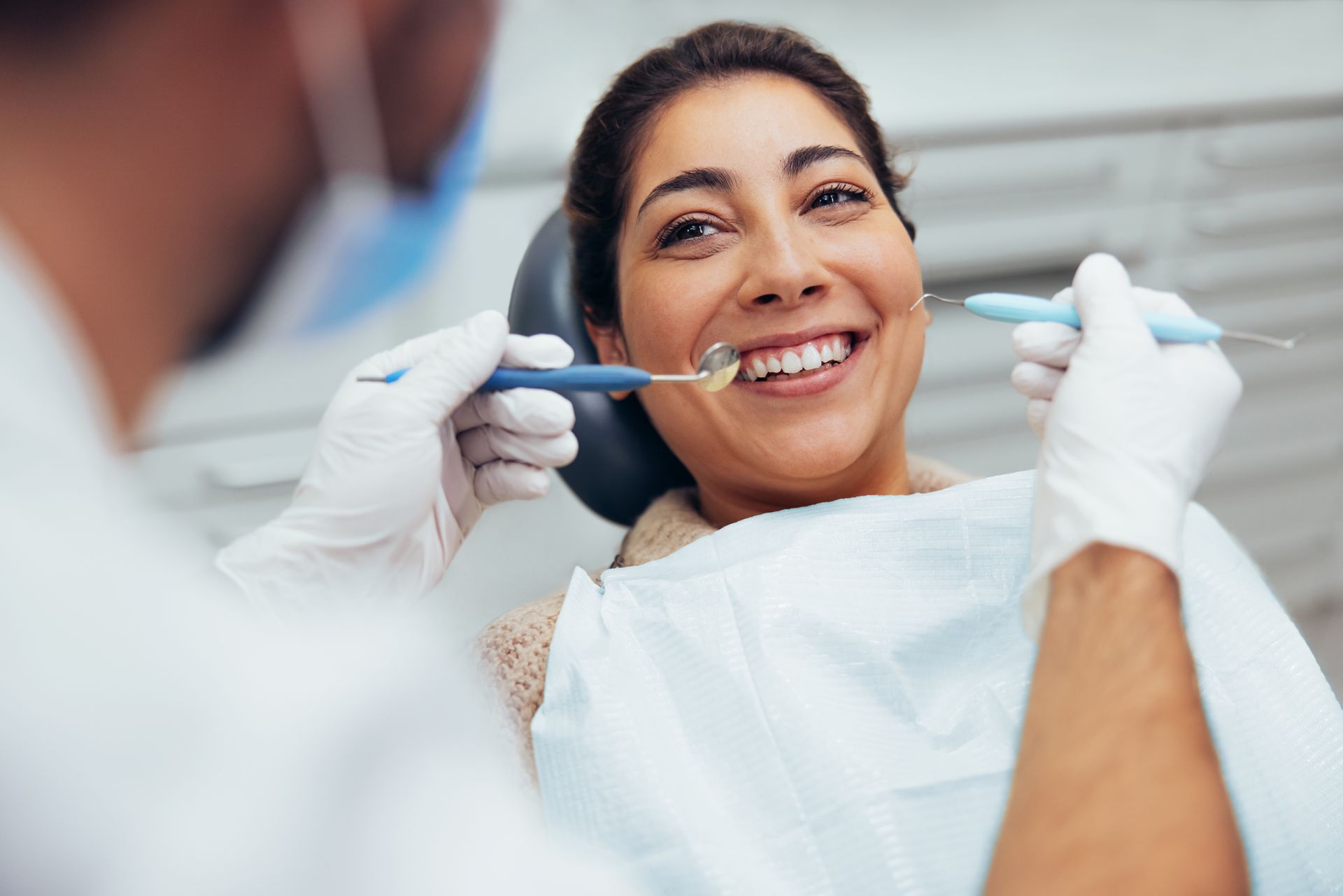 A woman is sitting in a dental chair while a dentist examines her teeth.