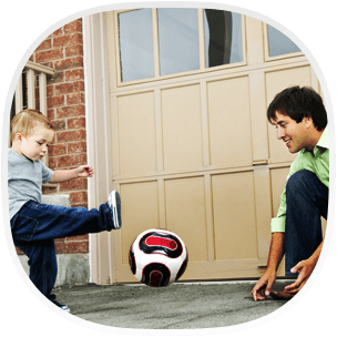 A man and child playing football in front of garage doors