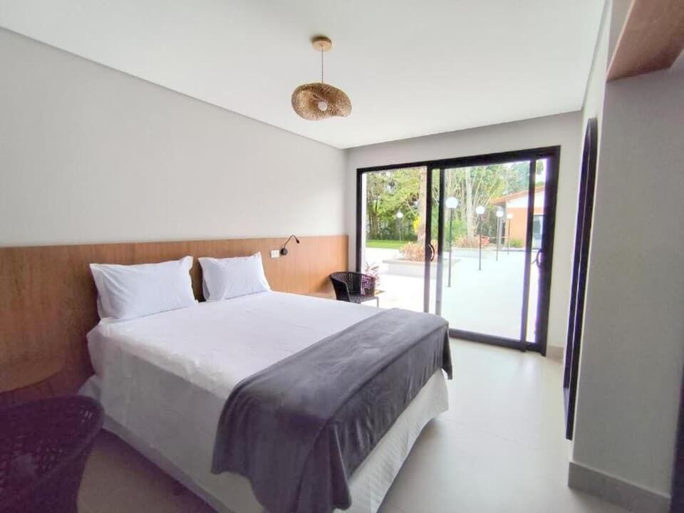 Quarto moderno com cama grande, cabeceira de madeira e portas de vidro deslizantes para um pátio.