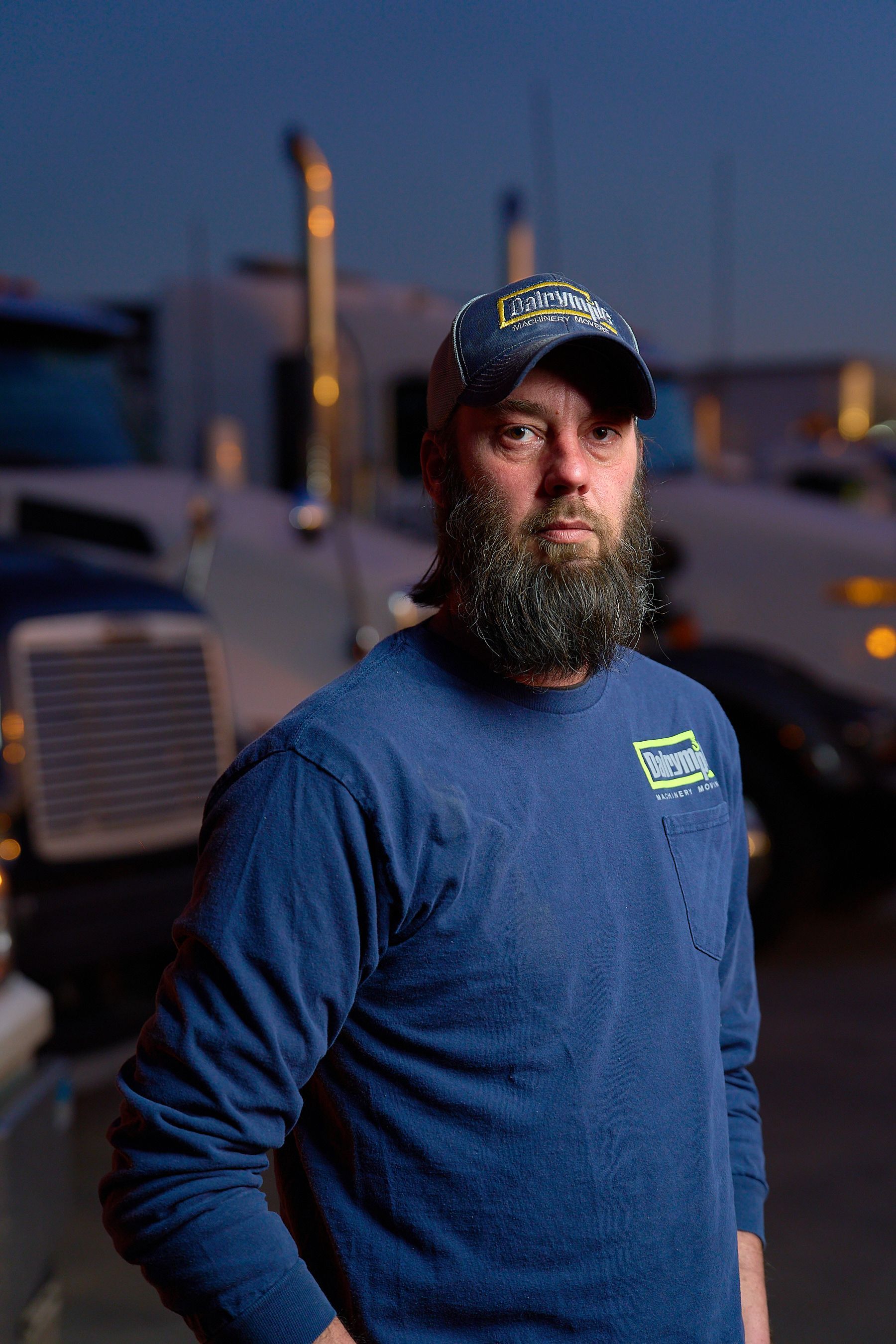 a man with a beard and hat is standing in front of a truck .