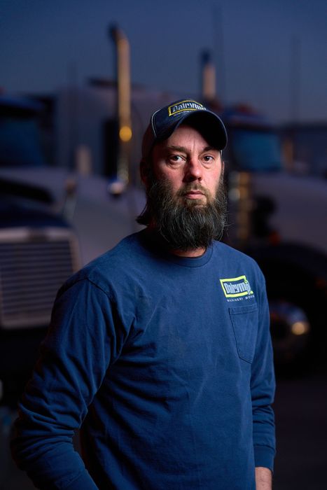 a man in a blue hoodie and hat is standing in front of a truck .