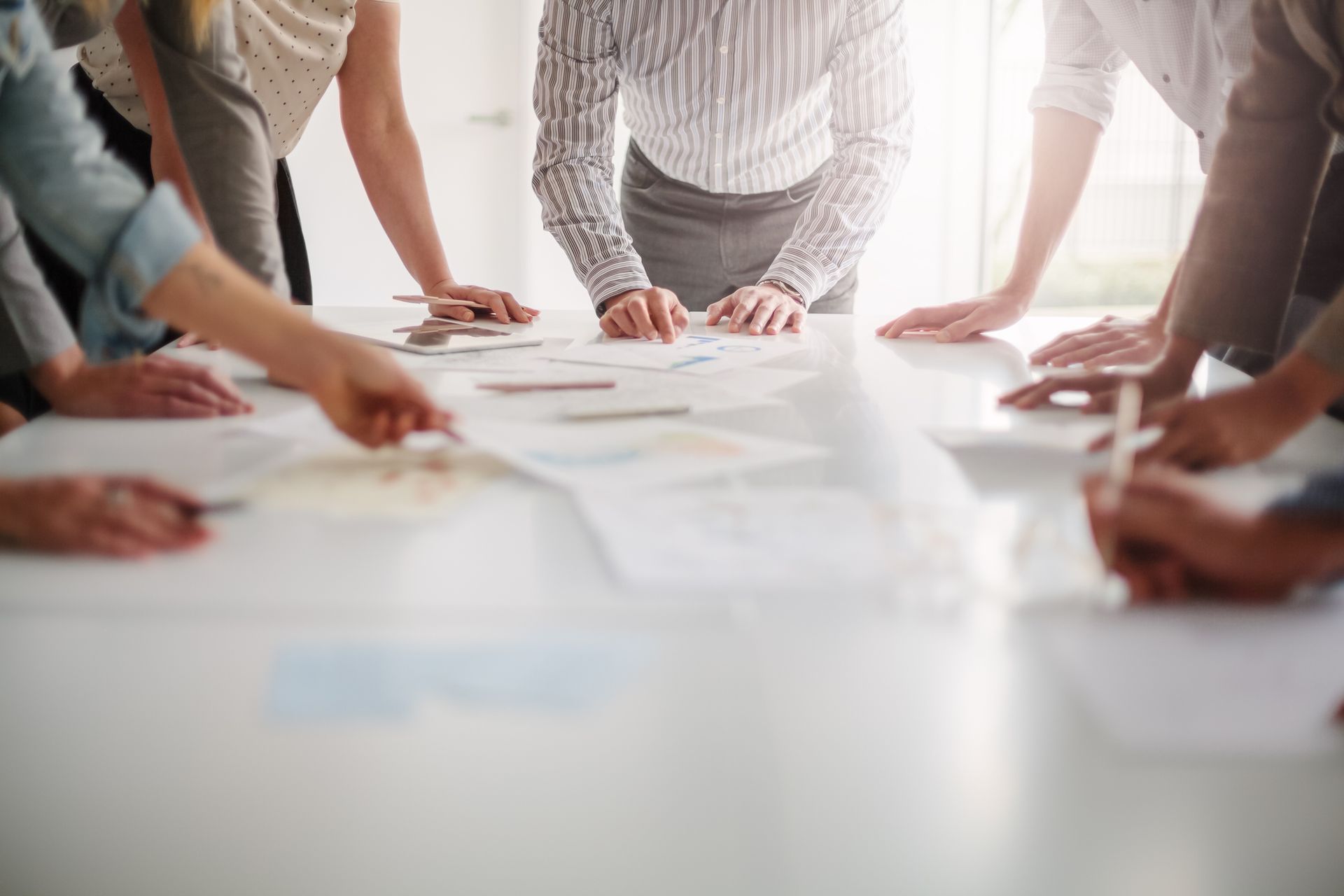People around a white table, reviewing documents, likely in a business meeting.