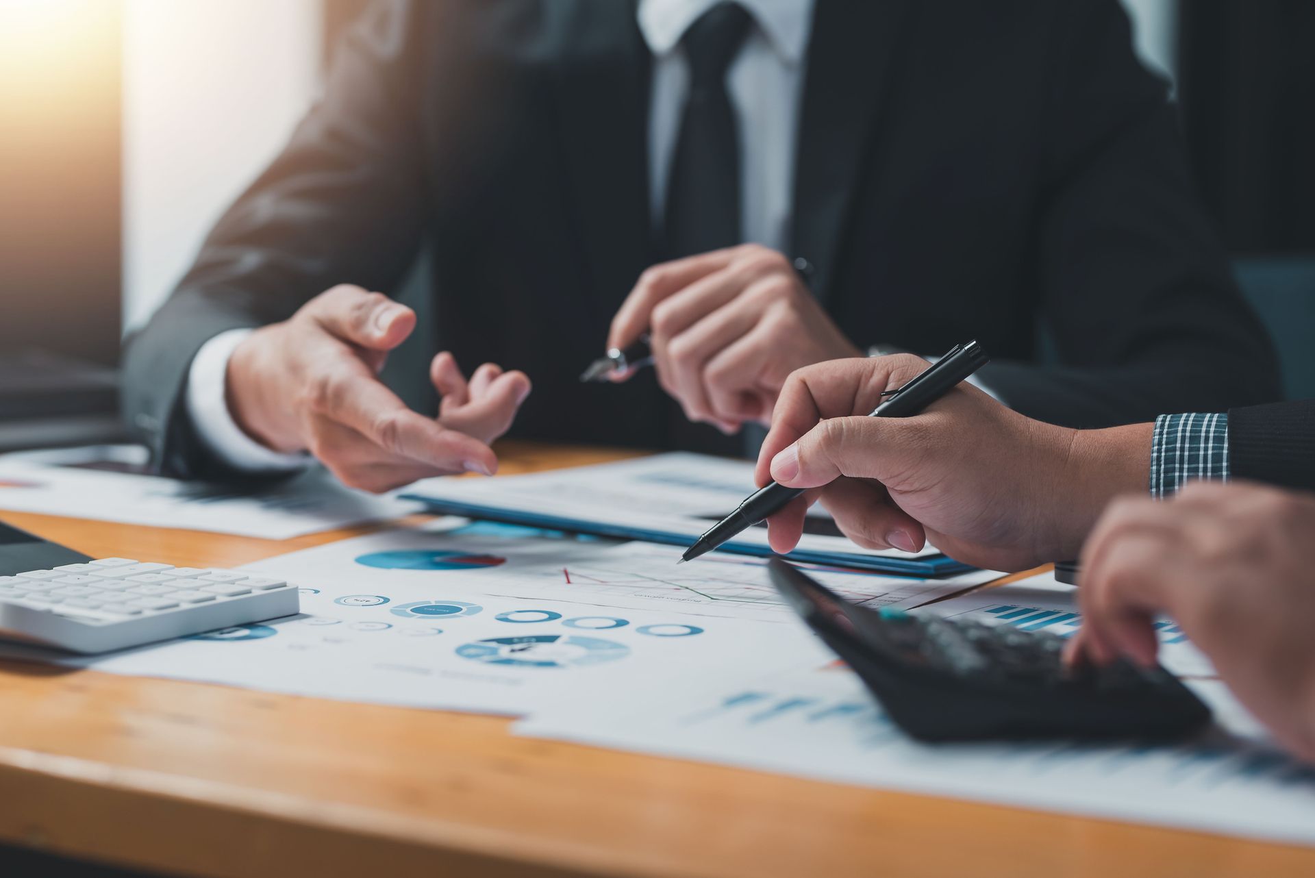 Two businesspeople in suits reviewing financial documents with calculator.