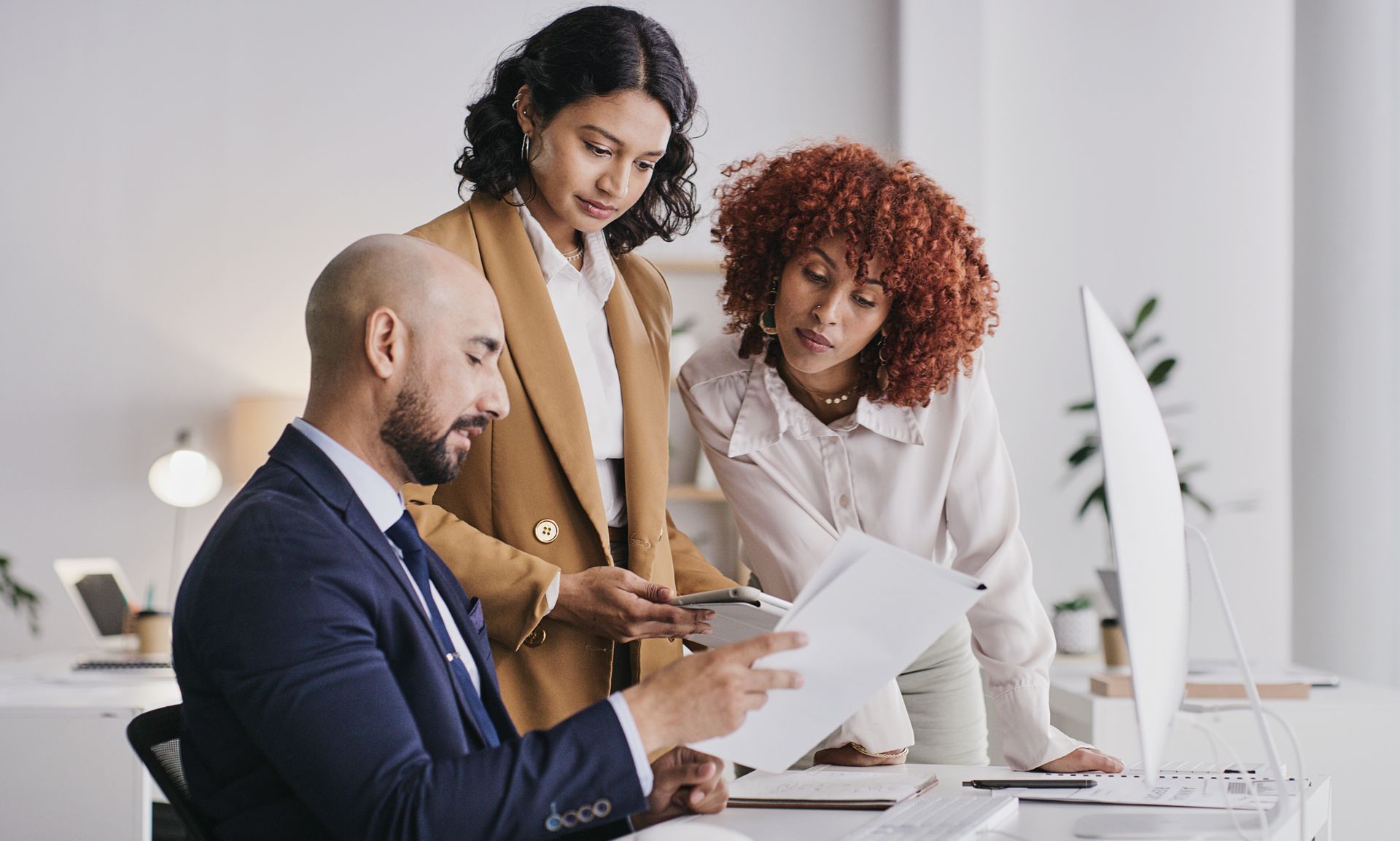 Three business colleagues reviewing documents at a desk in an office setting.