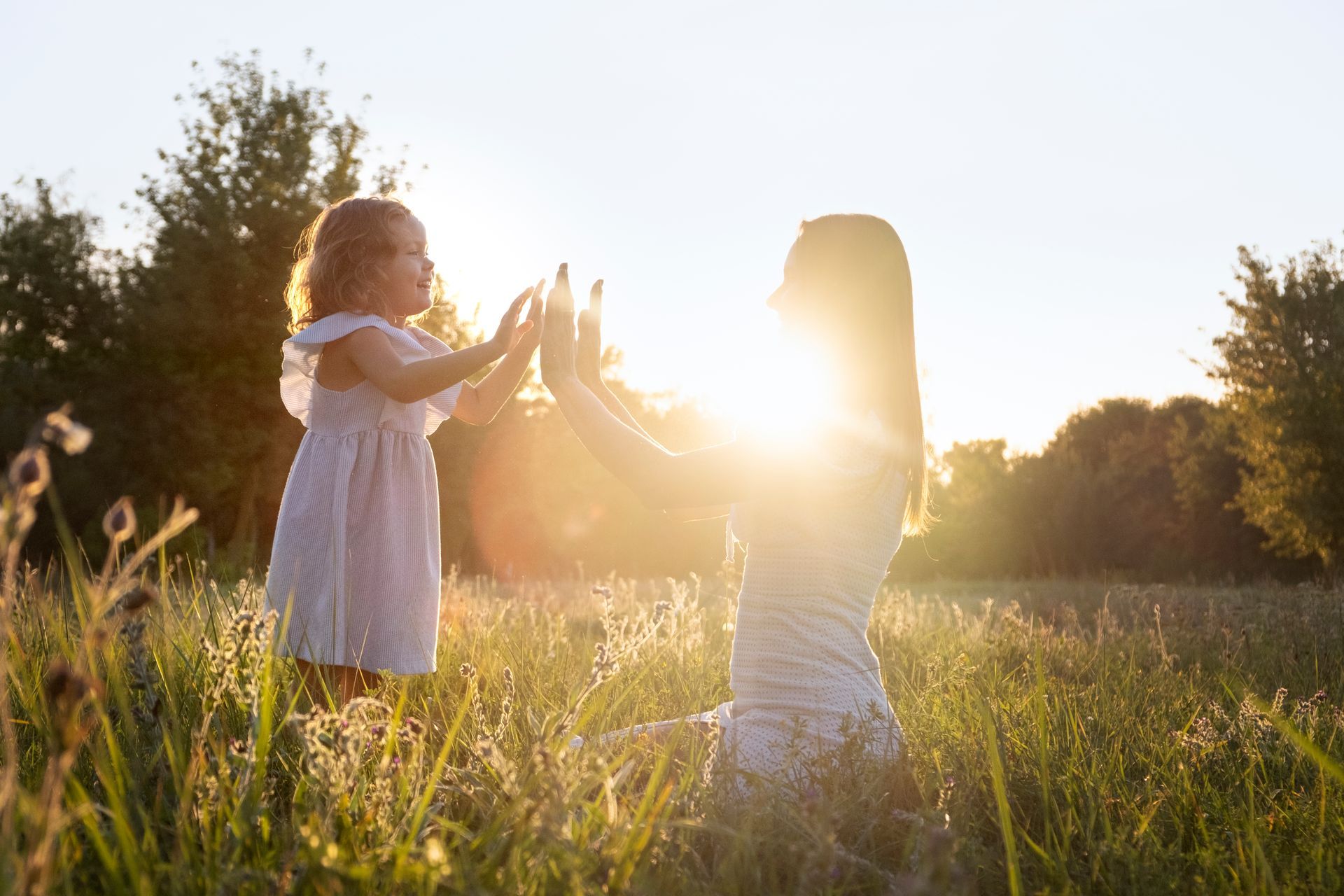Mujer y niño jugando a las palmaditas en un campo con la luz del sol brillando entre ellos.