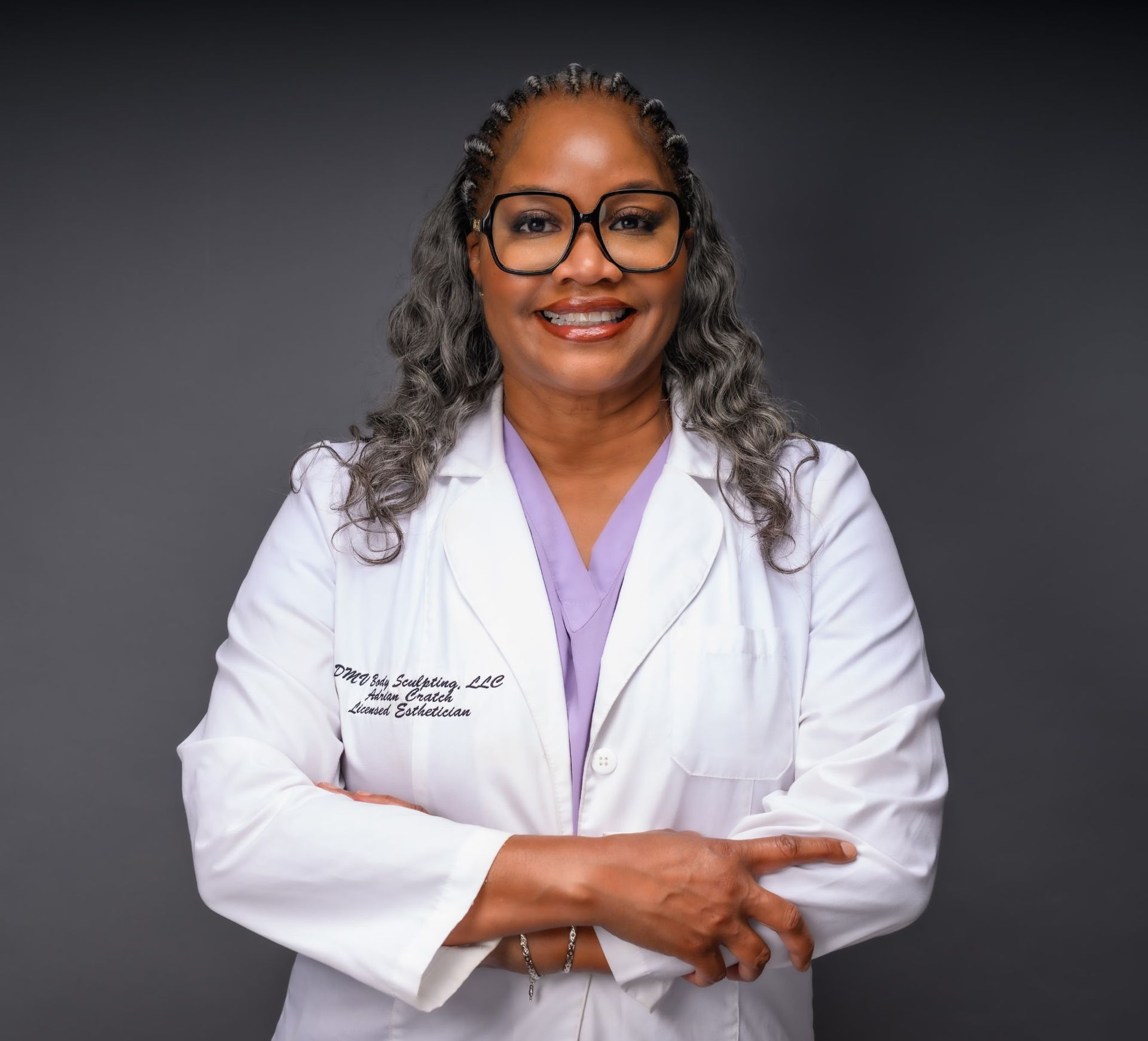 A smiling woman with blonde hair wearing a white lab coat. Gold hoops, neutral background.