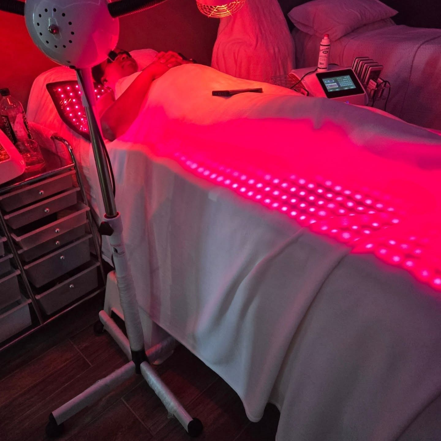 Person lying under red LED light therapy machine in a spa setting.
