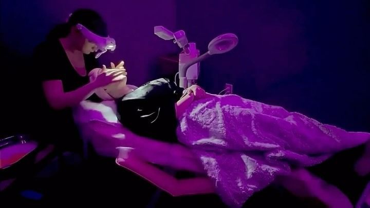 Woman receiving a facial treatment. Technician leans over her, lit by purple light, in a beauty clinic.