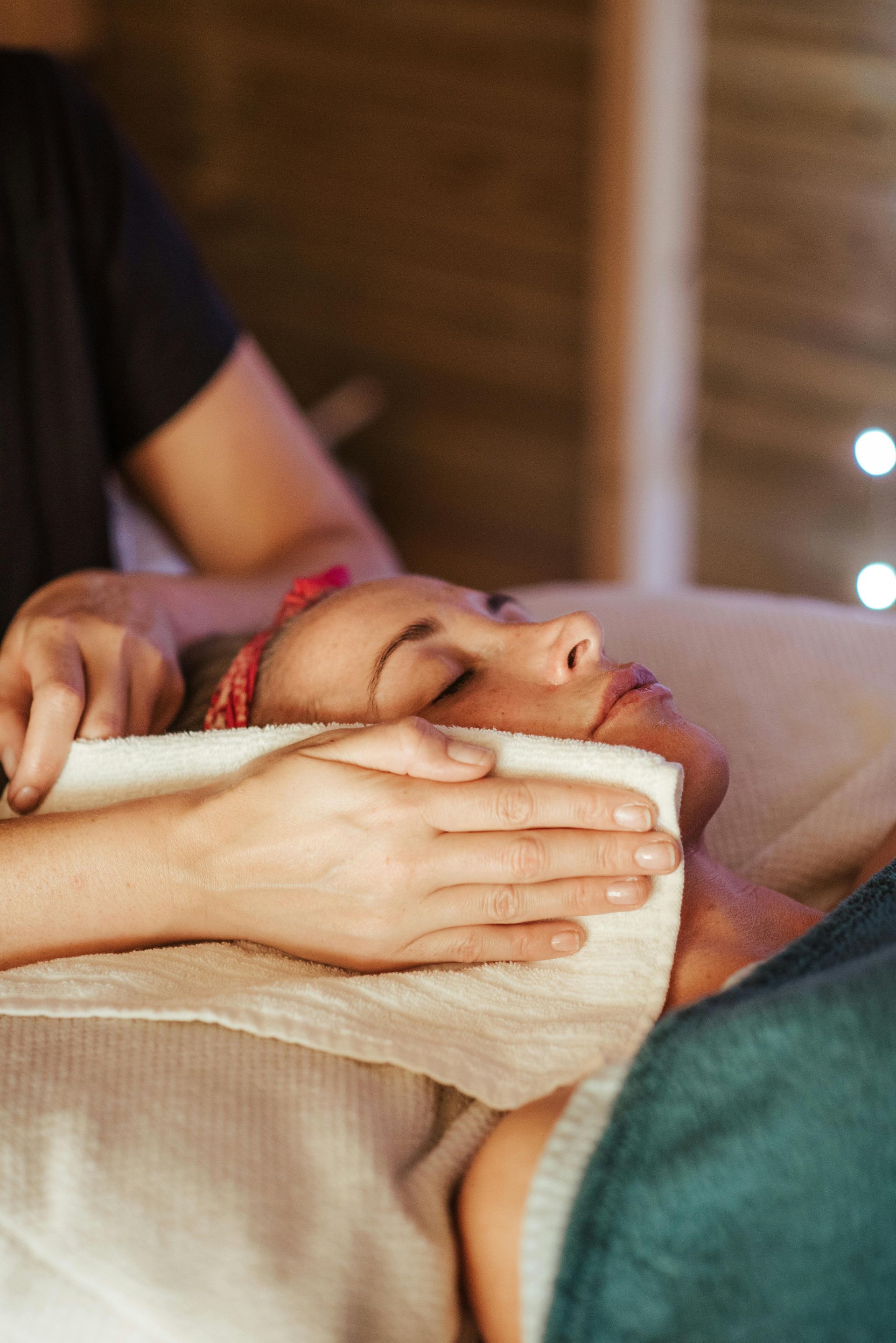 Woman receiving facial treatment, face covered with warm towel. Spa setting, soft lighting.