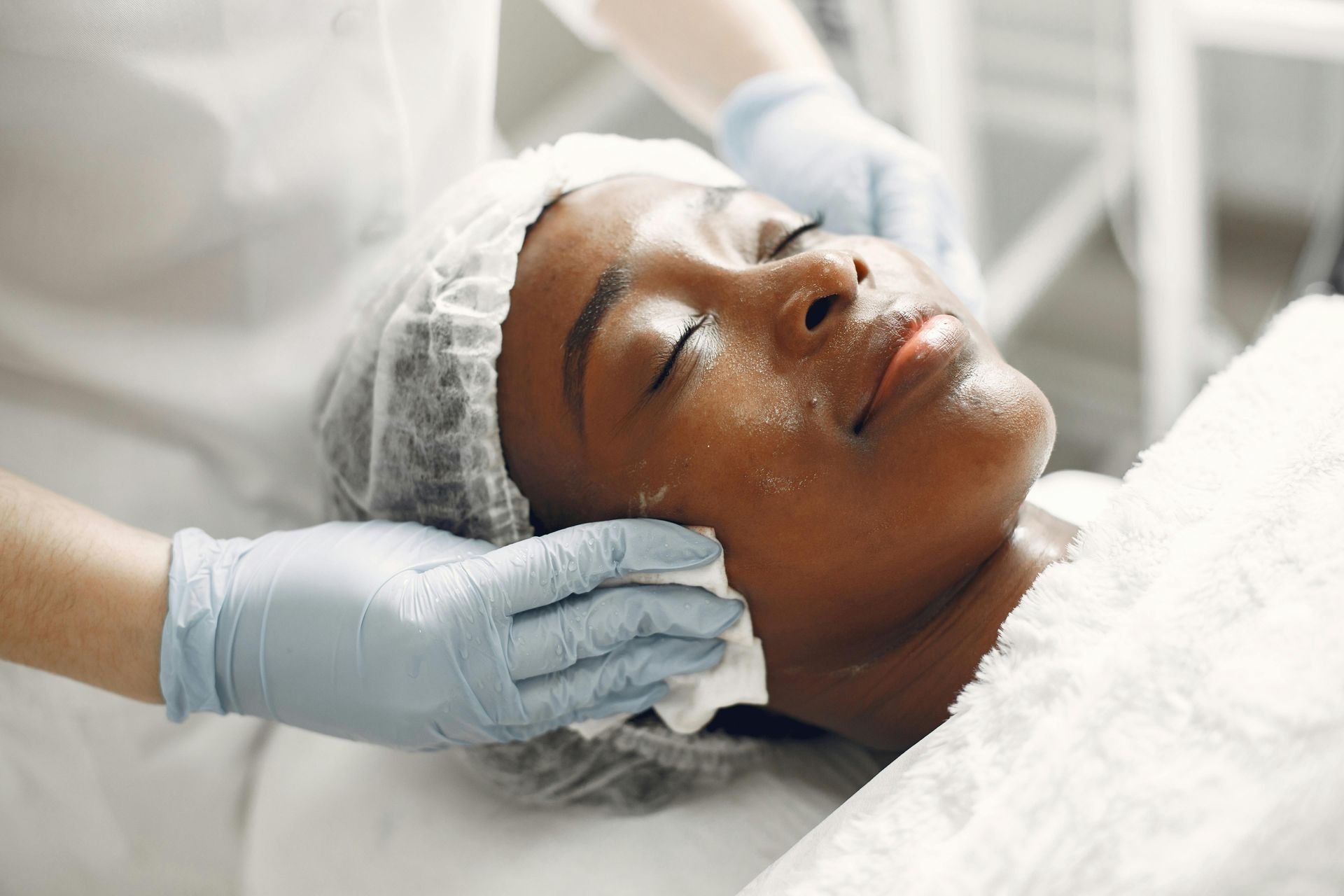 A woman receiving a facial treatment. A person in gloves gently cleans her face in a salon setting.