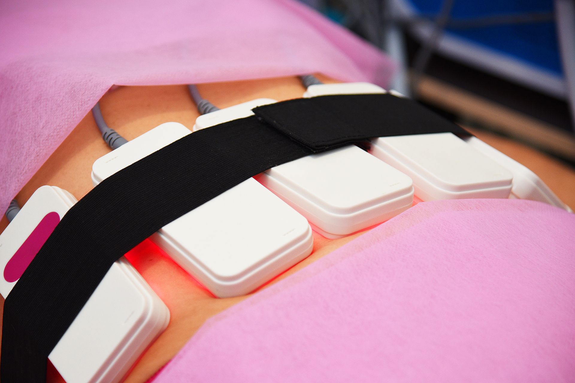 Person receiving laser fat reduction treatment. White applicators secured with a black strap on the abdomen. Red glow.