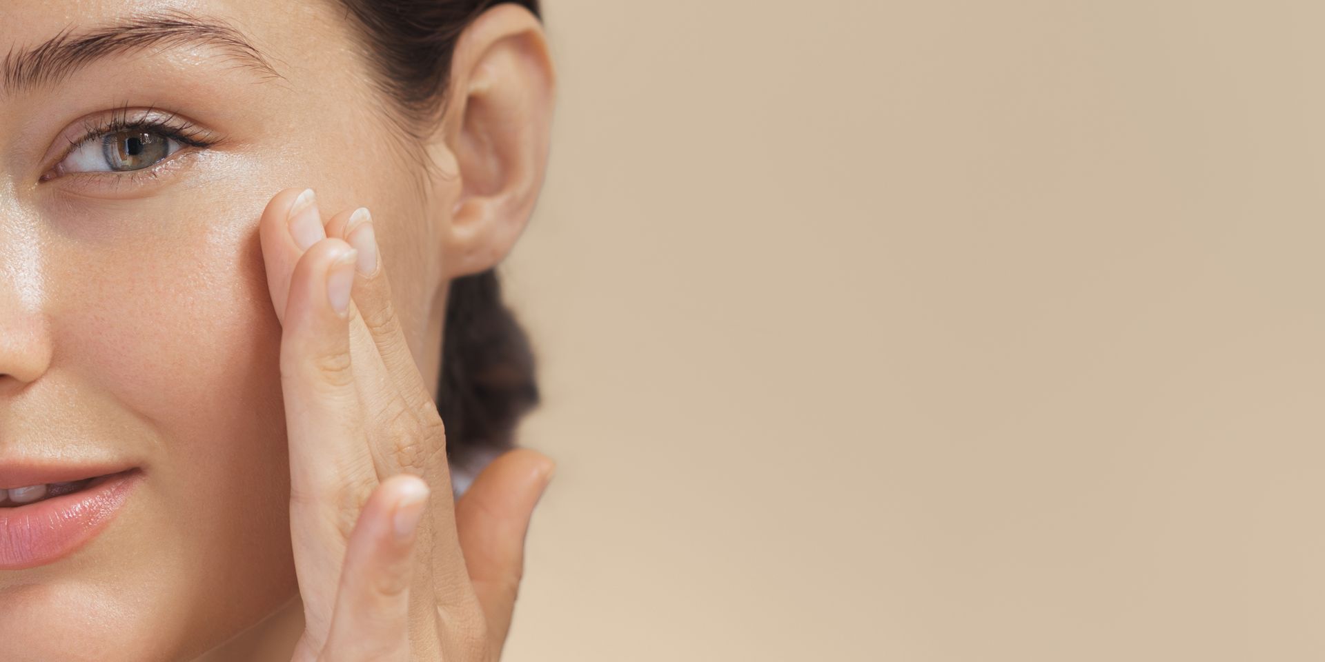 Woman touching her face with her hand, background is beige.