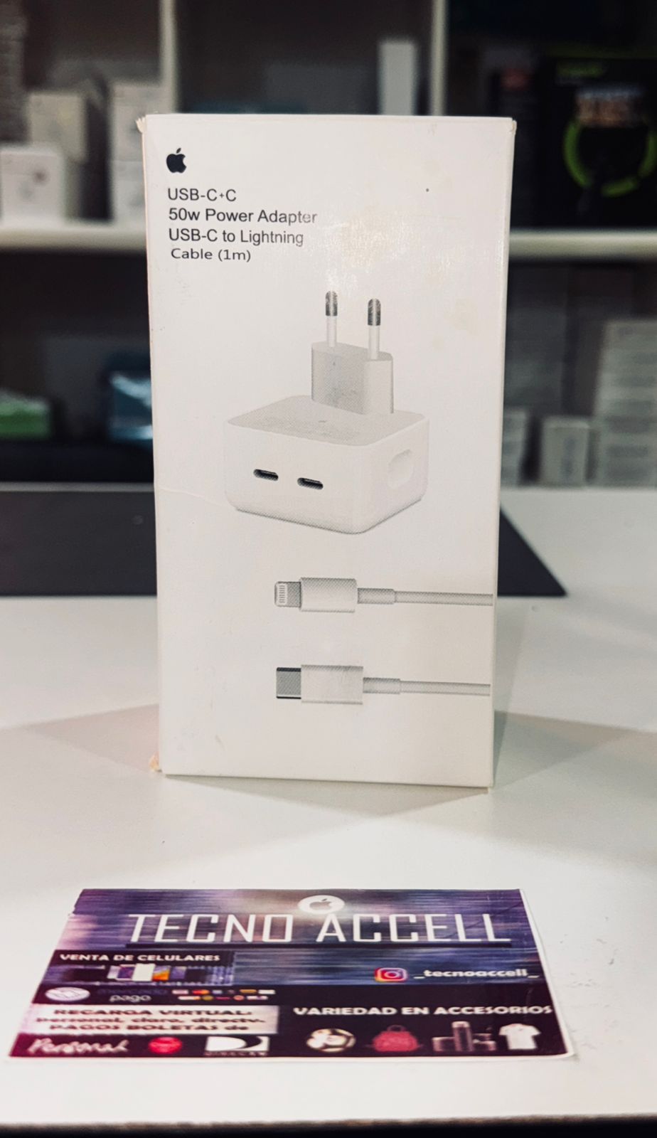 Adaptador de corriente USB-C de Apple en una caja blanca con un cable USB-C, sobre una mesa.