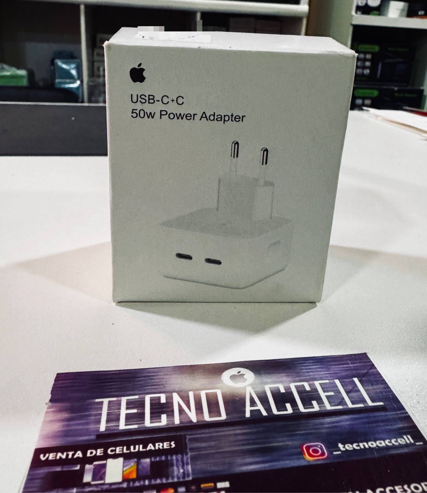 Caja del adaptador de corriente USB-C de 50 W de Apple sobre una mesa. Debajo, una tarjeta de presentación de