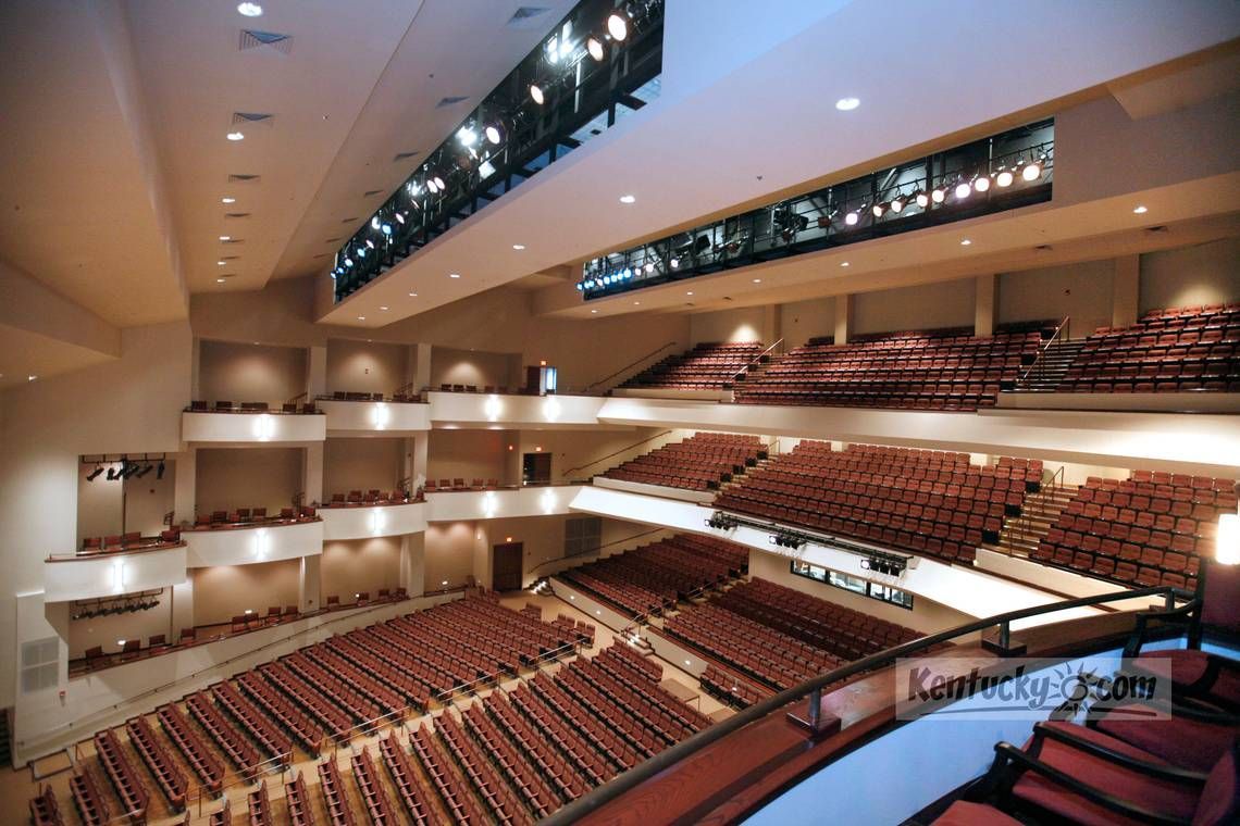 Auditorium with tiered seating, balconies, and stage lighting; red seats and beige walls.