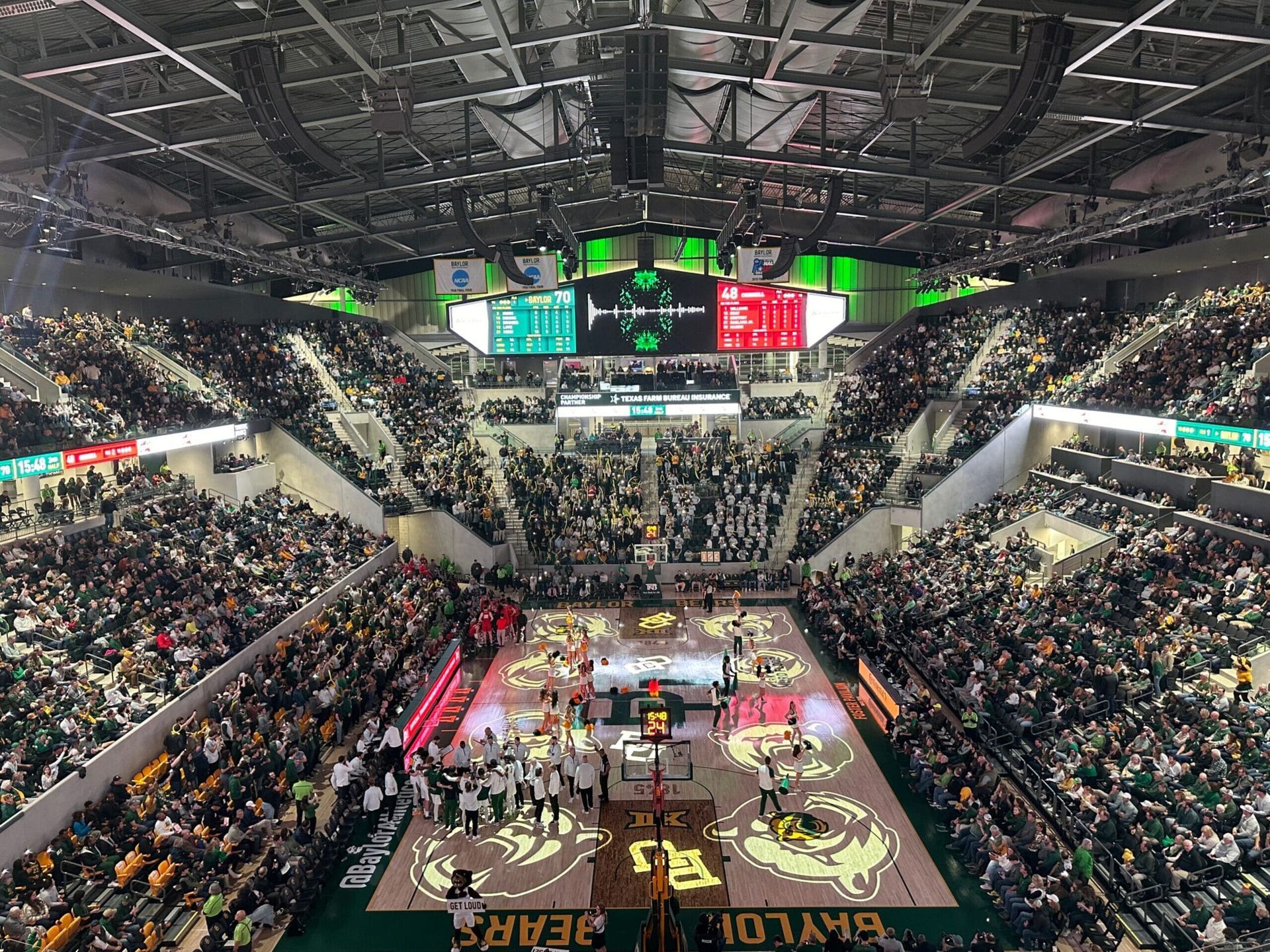 Stadium AV soltuions. A packed basketball arena with players on the court, fans cheering, and yellow foam sticks in the air.