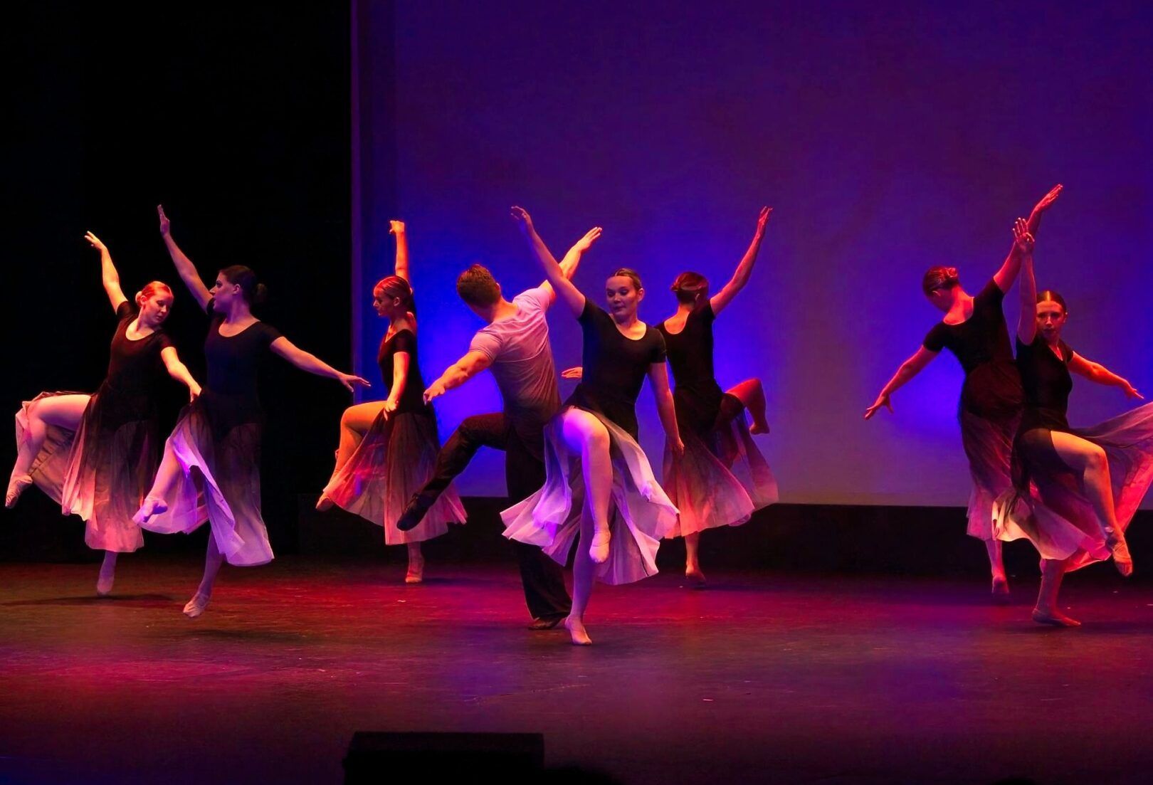 Auditorium AV solutions. Dancers in black and flowing skirts perform on stage under colorful lights.