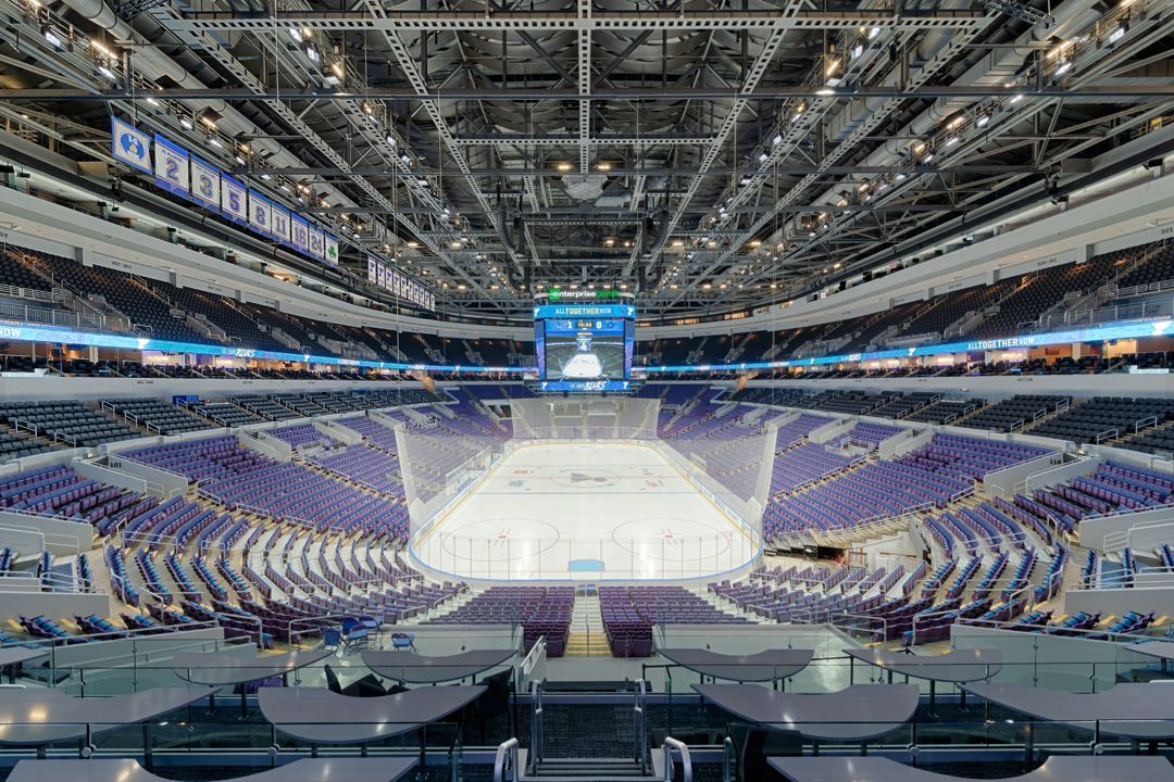 Stadium AV soltuions. An empty hockey arena with purple seats, bright ice rink, and a large scoreboard.