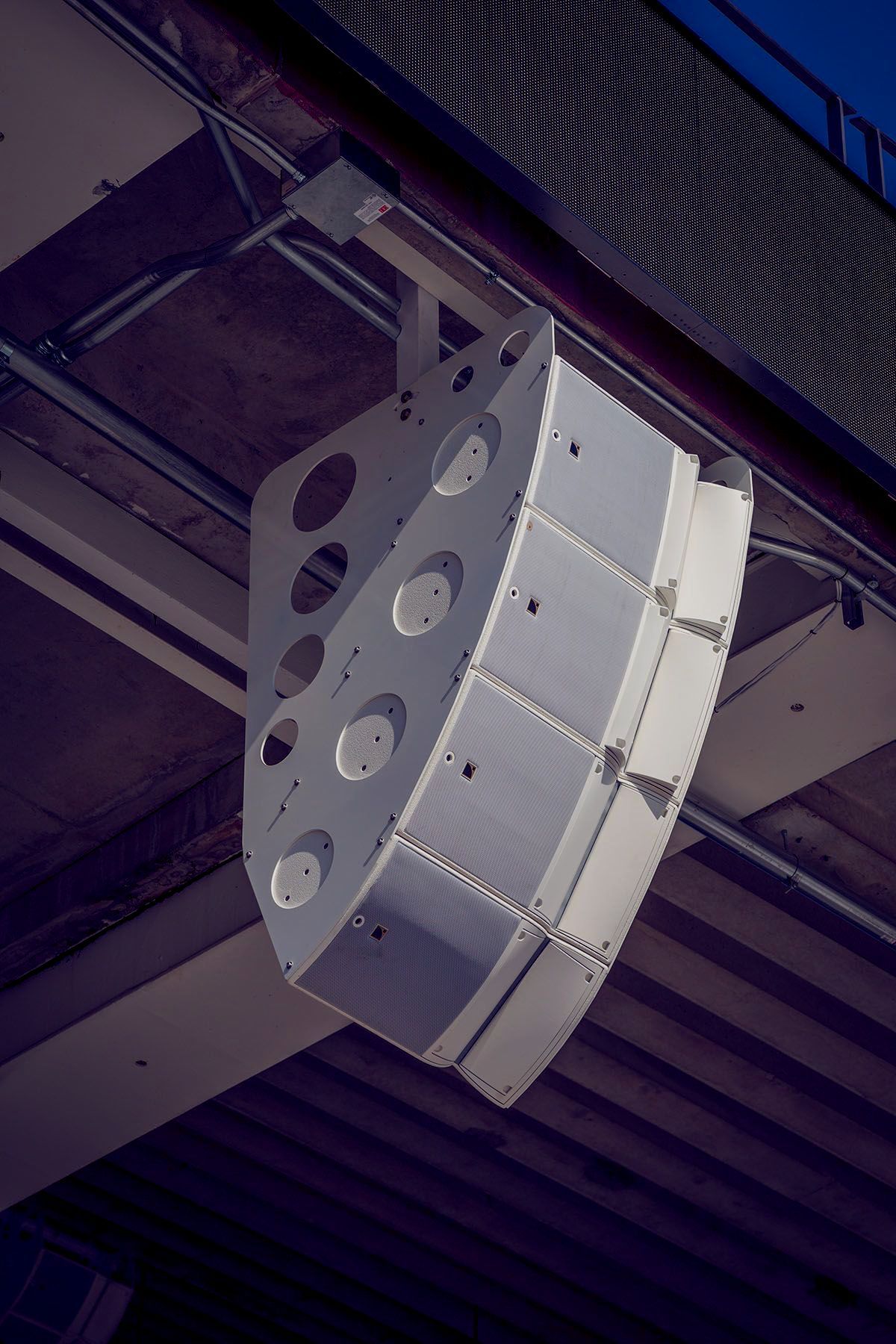 Stadium AV soltuions. White speaker system suspended from a dark ceiling.
