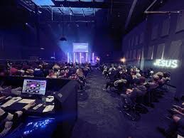 House of Worship AV solutions. Audience in a dark auditorium; a stage with blue and purple lights, a 