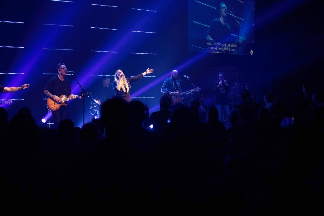 House of Worship AV soltuions. Band performing on stage with blue lighting, singer with arms raised, crowd in foreground.