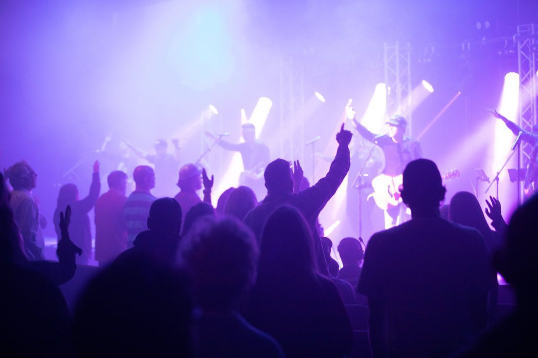Concert stage with band, vertical lights, snowflakes, and audience; blue and white lighting.