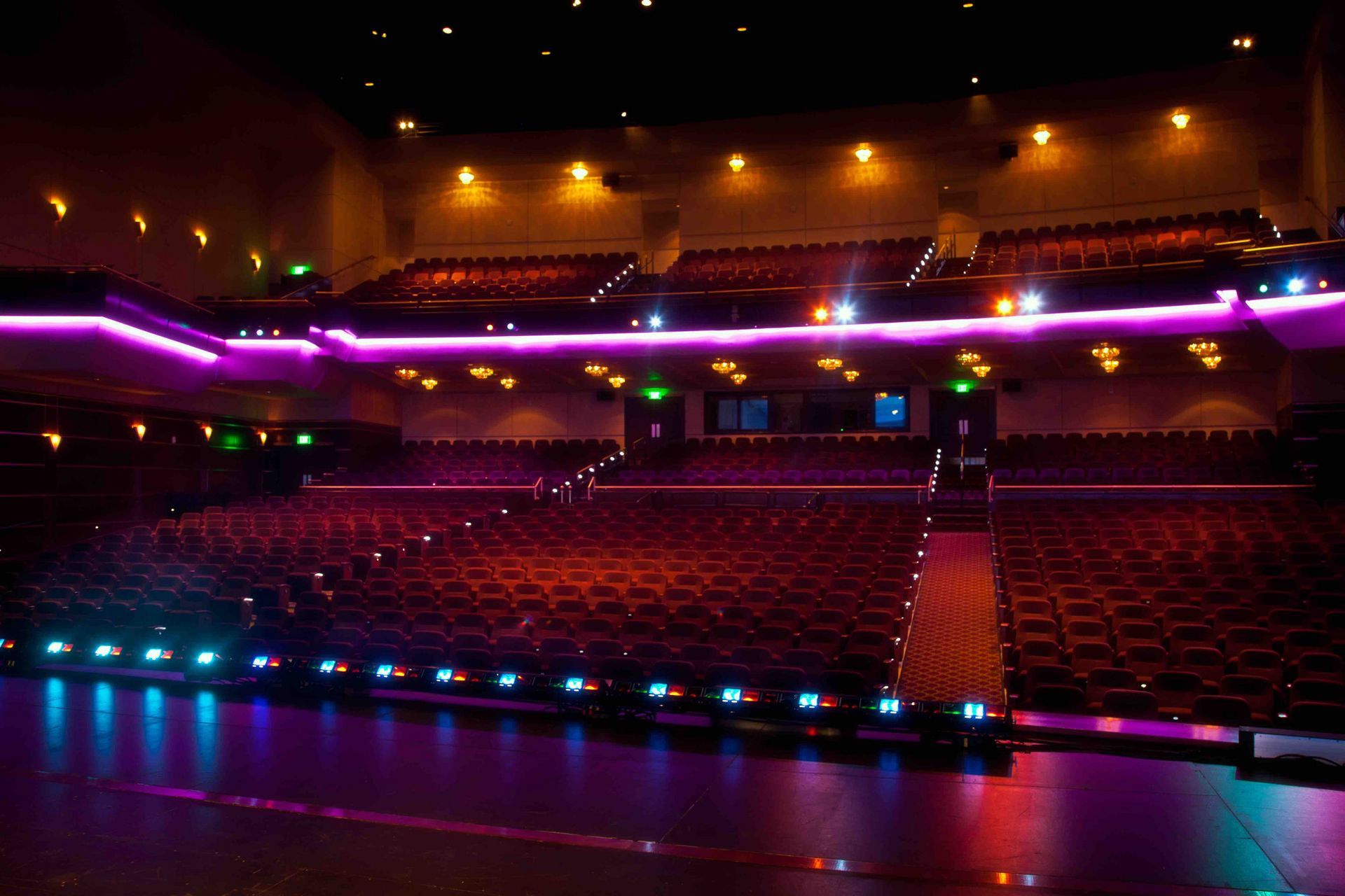 Auditorium AV solutions. Empty theater auditorium with rows of seats, lit by colorful stage lights.
