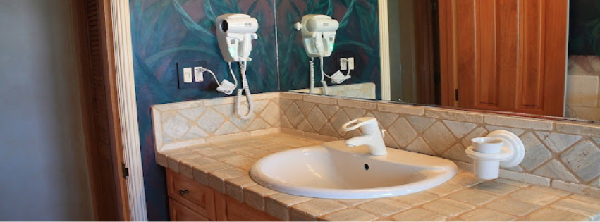 A bathroom with a sink , mirror and hair dryers.